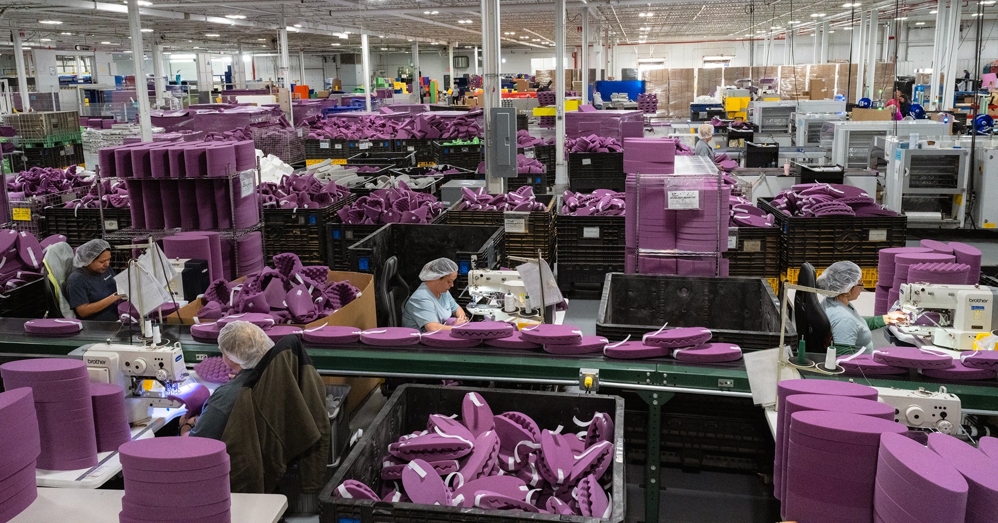 Envirolite Foam Manufacturer Factory interior with workers assembling purple products on a conveyor belt.